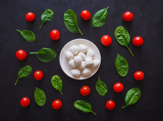 Italian mozzarella cheese, cherry tomatoes and spinach leaves on a black table. Pattern.