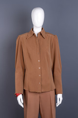 Mannequin in female brown shirt. Women long sleeve blouse and trousers on mannequin, grey background. Ladies office style.