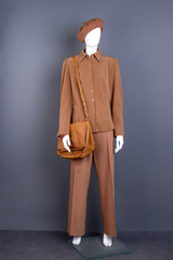 Full length mannequin in stylish outfit. Dummy with brown women clothes and handbag, grey background.