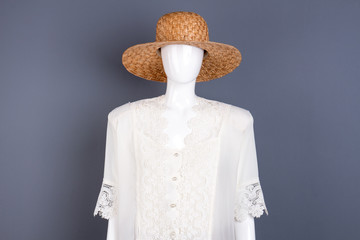 Straw hat and white blouse on mannequin. Dummy in elegant female clothing, grey background.