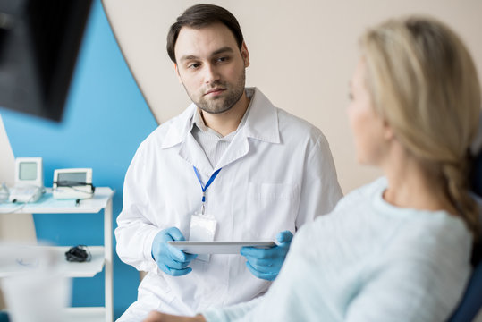 Confident man in white gown and gloves having talk to woman working in dentistry cabinet. 