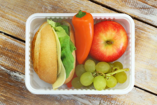 Healthy school lunch containing cheese roll, fresh fruit and yellow pepper
