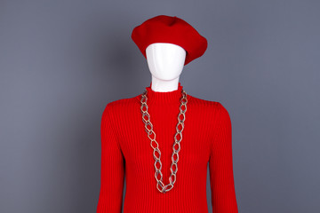 Red sweater, beret and chain. Mannequin dressed in red hat and pullover, grey background. Feminine fashion attire.