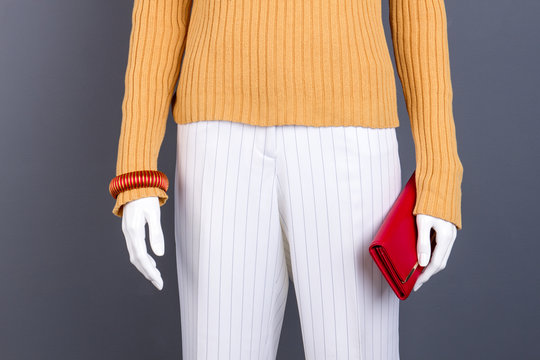 Female mannequin with red bracelet and wallet. Dummy dressed in yellow pullover and white trousers. Ladies fashion clothes and accessories store.