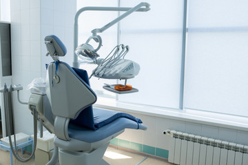 Blue colored seat and working objects of dentist placed in light modern office. 