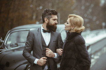 Couple in love on romantic date. Bearded man and sexy woman in fur coat. Retro collection car and auto repair by mechanic driver. Travel and business trip or hitch hiking. Escort of girl by security.