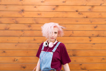 Bunny girl with a fun pink hairstyle, headphone and stylish clothes on the background of a wooden wall. Portrait of a stylish hipsters girl on a wooden background