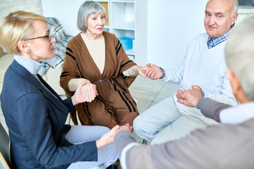 Elderly patients sitting in circle with therapist and holding hands on consultation in assisted living home. 