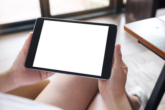 Mockup image of a woman sitting cross legged and holding black tablet pc with blank white desktop screen