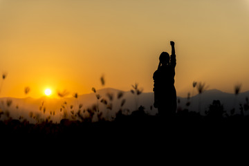 Silhouette woman at sunset standing elated with arms raised up above her head.