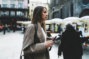 Office worker female in casual clothes going to the office with a take away coffee cup and a newspaper after lunch. Hipster girl holding coffee cup and new magazine while crossing the street.