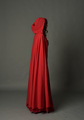 full length portrait of woman wearing red fantasy costume with cloak, standing pose on grey studio...