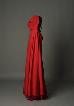 full length portrait of woman wearing red fantasy costume with cloak, standing pose on grey studio background.