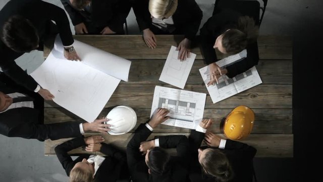 Business people discuss construction blueprint, hardhat on office table