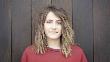Fototapeta premium A young cute casual brunette girl in a red sweatshirt on a wooden brown background