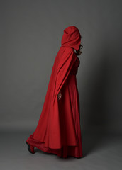Naklejka na ściany i meble full length portrait of woman wearing red fantasy costume with cloak, standing pose on grey studio background.