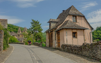 Fototapeta na wymiar Conques, Midi Pyrenees, France - July 31, 2017: Typical house at the entrance to the village of Conques with the Cathedral of Sainte Foy at the back