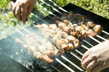 barbecue on the grill in the summer outdoors, hands turn the skewer for even roasting