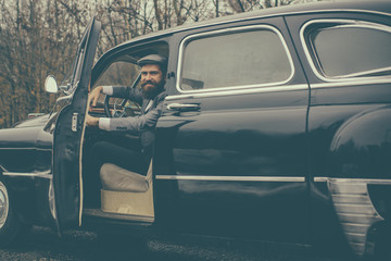 Call boy in vintage auto. Bearded man in car. Retro collection car and auto repair by mechanic driver. Travel and business trip or hitch hiking. Escort man or security guard