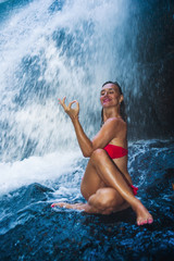 young happy and attractive woman doing yoga exercise posing under beautiful tropical waterfall getting wet smiling happy in meditaton