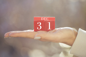 the woman is holding a red wooden calendar. Red wooden cube shape calendar for DEC 31 with hand 