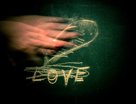 On the chalkboard written "Love" and painted heart. The female hand erases the inscription.
