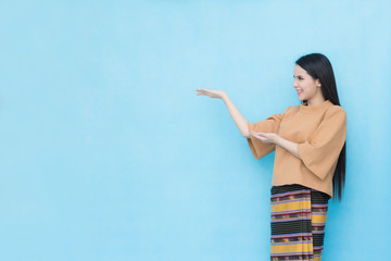 Portrait of asian young girl in traditional thai dress shows blank sign isolated on blue sky background..