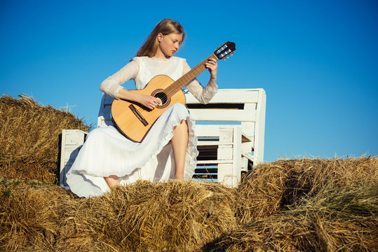 Fashion musician in white dress on sunny nature. Woman guitarist perform music concert. Albino girl hold acoustic guitar, string instrument. Sensual woman play guitar on wooden bench