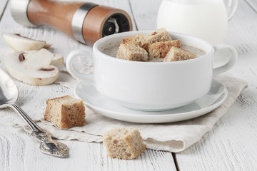 Mushroom soup in white pot, on napkin, on wooden background
