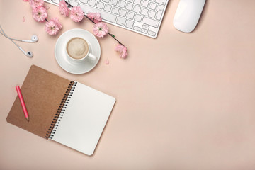 White cup with cappuccino, sakura flowers, keyboard, alarm clock, notebook on a pastel pink...