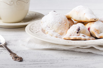Delicious rustic pastries filled with berry on a ceramic plate on a wooden background.