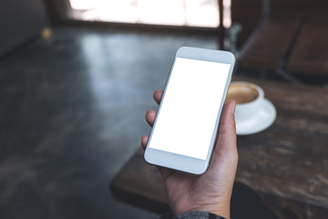Mockup image of a woman's hand holding white mobile phone with blank desktop screen with coffee cup on wooden table in cafe