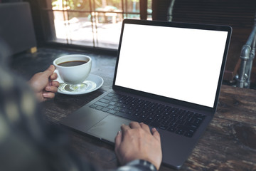 Fototapeta premium Mockup image of a woman using laptop with blank white desktop screen while drinking hot coffee in cafe