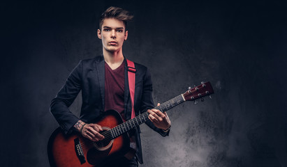 Obraz premium Stylish young musician with stylish hair in elegant clothes, playing on an acoustic guitar.