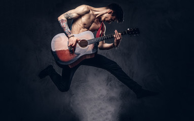 Fototapeta na wymiar Handsome shirtless young musician playing guitar while jumping.