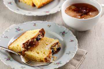 sliced cake with almonds and blueberries on a white ceramic plate with a Cup of tea