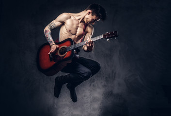 Handsome shirtless young musician playing guitar while jumping.