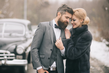 Toward adventure! Happy loving couple is relaxing and enjoying road trip. Young woman, man and vintage car on winter nature background. Christmas holidays times