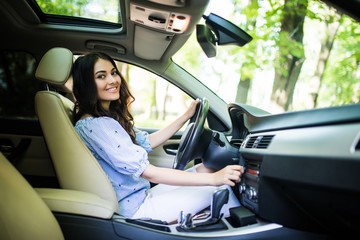 Naklejka premium Young smiling woman driver with fastened safety seat belt turning on or tuning vehicle audio, finding a playlist for a pleasant and comfortable ride