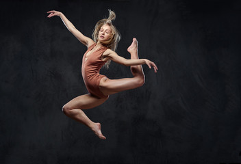Fototapeta na wymiar Young graceful ballerina dances and jumps in a studio. Isolated on a dark background.
