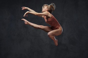 Fototapeta na wymiar Young graceful ballerina dances and jumps in a studio. Isolated on a dark background.