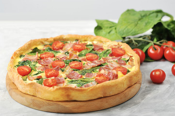 Classic French pie kish. Filling with cream, chicken eggs, spinach and bacon. In the frame, a bunch of green spinach and cherry tomatoes. Close-up.