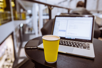 yellow coffee cup on table. laptop with cellphone on background. freelancer concept