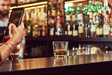 Cropped image of a customer of the bar takes a picture on the phone of a glass of alcohol on a bar counter.