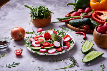Wooden plate with vegetables for a vegetarian salad on white textured background, close-up, selective focus