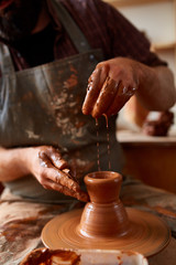 Close-up hands of a male potter in apron making a vase from clay, selective focus