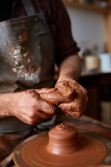 Close-up hands of a male potter in apron molds bowl from clay, selective focus