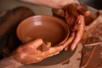 A potter paints a clay plate in a white in the workshop, top view, close-up, selective focus.