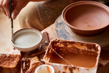 A potter paints a clay plate in a white in the workshop, top view, close-up, selective focus.