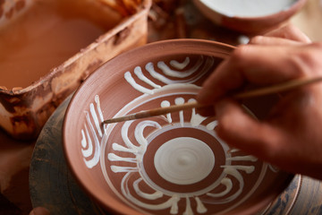 A potter paints a clay plate in a white in the workshop, top view, close-up, selective focus.